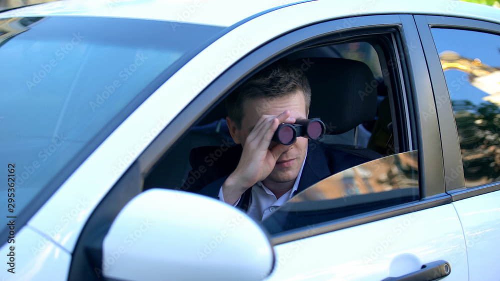 Man in suit spying from car using binoculars, private detective investigation Man in suit spying from car using binoculars, private detective investigation