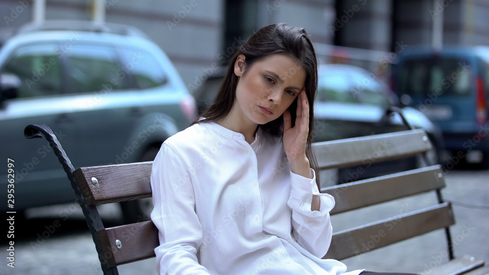 Exhausted woman sitting on bench, suffering from migraine pain, health problem Exhausted woman sitting on bench, suffering from migraine pain, health problem