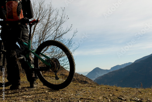 man with an electric bicycle, e-bike, ebike, looking mountains covered by the first snow, autumn, sunset, Piedmont, Ossola Valley, Italy