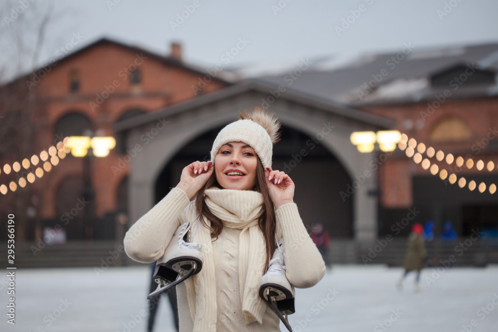 Fototapeta premium Charming young woman in the Park near the ice rink. Smiling brunette with skates