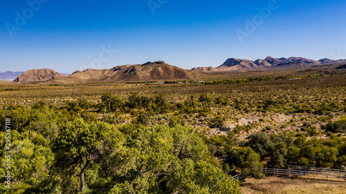 Beautiful view of famous Spring Mountain Ranch State Park near Las Vegas and Red Rock Canyon, Nevada during autumn with pink and red rock mountains, blue sky, green trees and grass, and purple hills