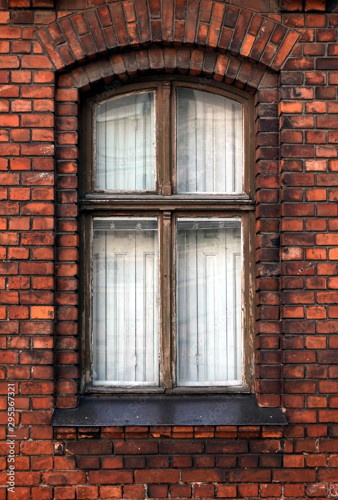 Tightly closed vintage vertical wooden window in red brick wall as fragment of old living house front view closeup
