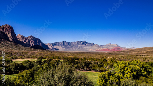 Beautiful view of famous Spring Mountain Ranch State Park near Las Vegas and Red Rock Canyon, Nevada during autumn with pink and red rock mountains, blue sky, green trees and grass, and purple hills