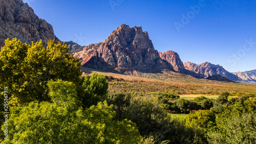 Beautiful view of famous Spring Mountain Ranch State Park near Las Vegas and Red Rock Canyon, Nevada during autumn with pink and red rock mountains, blue sky, green trees and grass, and purple hills