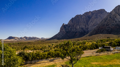 Beautiful view of famous Spring Mountain Ranch State Park near Las Vegas and Red Rock Canyon, Nevada during autumn with pink and red rock mountains, blue sky, green trees and grass, and purple hills