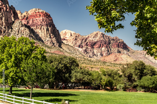 Beautiful view of famous Spring Mountain Ranch State Park near Las Vegas and Red Rock Canyon, Nevada during autumn with pink and red rock mountains, blue sky, green trees and grass, and purple hills