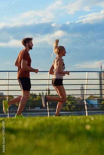 Fototapeta Naklejka Na Ścianę i Meble -  Modern woman and man jogging / exercising in urban surroundings near the river.