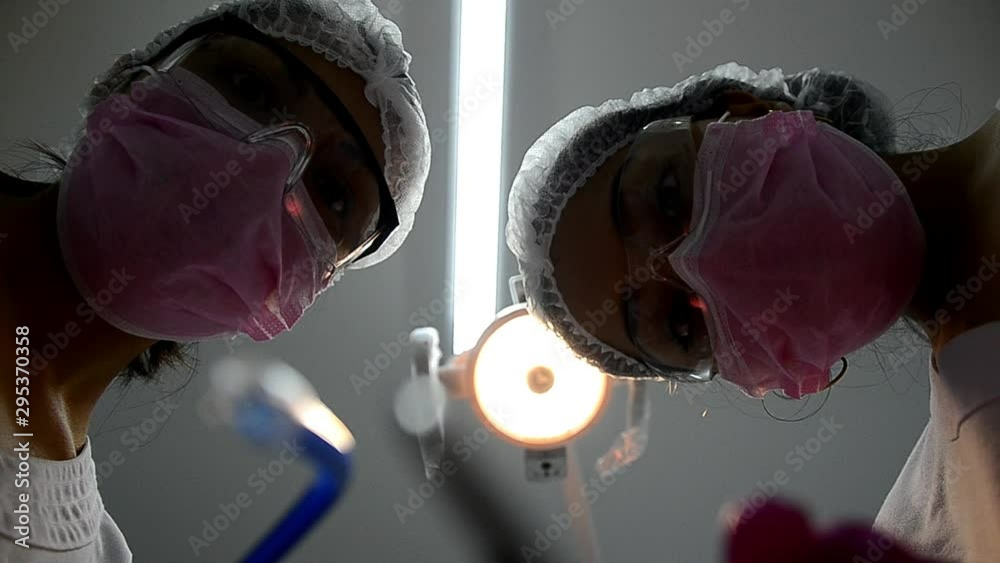 Bottom view of two women dentists in surgical mask holding tools and looking at camera. Patient point of view to dentist.