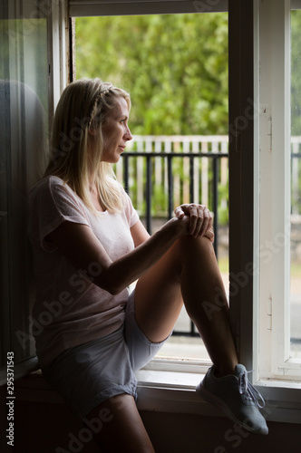 Beautiful long haired blonde middle age woman sits in window, and looks at street.