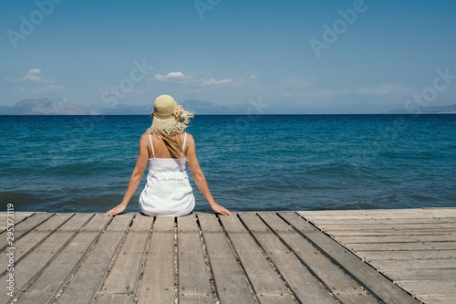 Woman in hat sitting and looking at the blue sea. Girl in white dress looking into the distance, summer mood. Relax on the beach