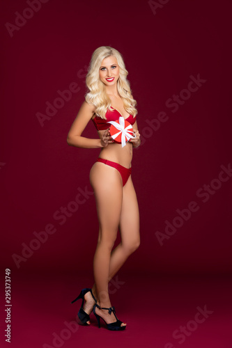 Beautiful blond woman in red swimsuit holding Christmas gift. Fashion model posing in studio.