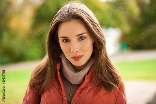 Young stylish woman in a salmon down jacket posing on a background of autumn park photo