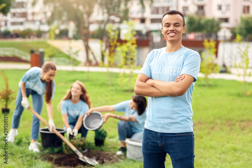 Volunteering. Young people volunteers outdoors planting trees guy standing crossed arms close-up smiling happy blurred background