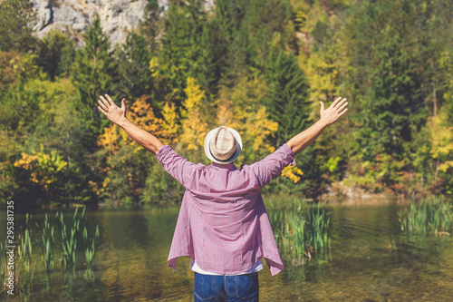 Fashionable traveler with hands up against lake or river and wood forest trees. photo