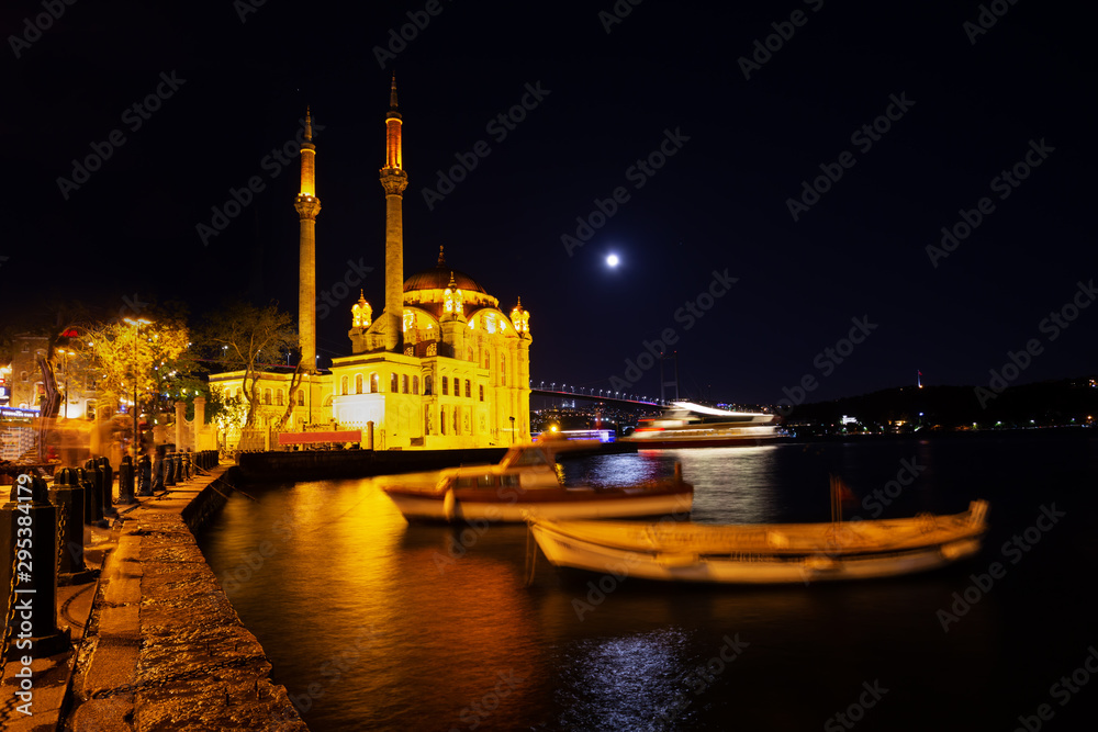 Ortakoy Mosque and embankment with swinging boats on background of Bosphorus Bridge at night