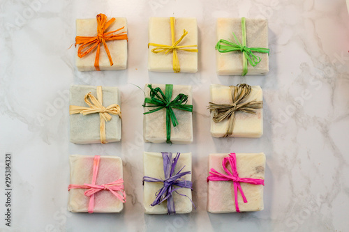 handmade organic craft soap in gift wax wrapping  paper with multi colored eco raffia ribbons on marble surface with space for text. Present gift soap flat lay top view