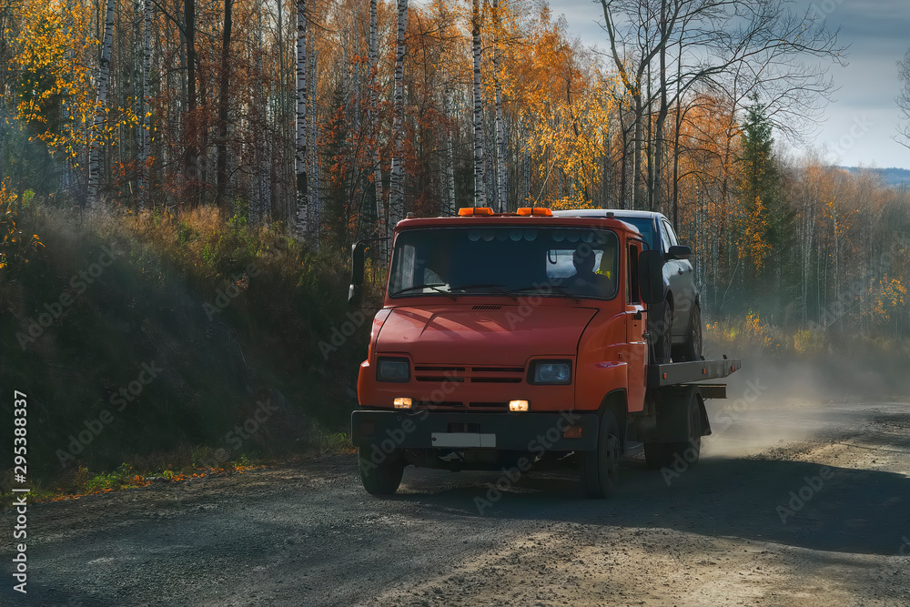 Tow truck rides along a forest road against the backdrop of an autumn forest.