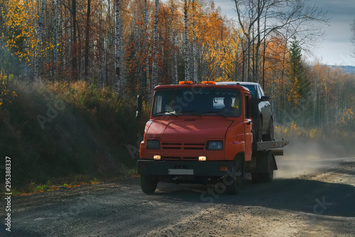 Tow truck rides along a forest road against the backdrop of an autumn forest.