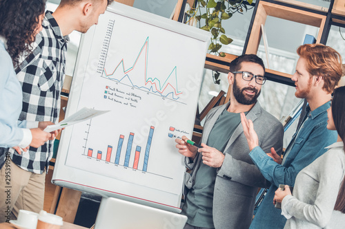 Startupers working together at office standing near board duscussing data chart smiling joyful photo