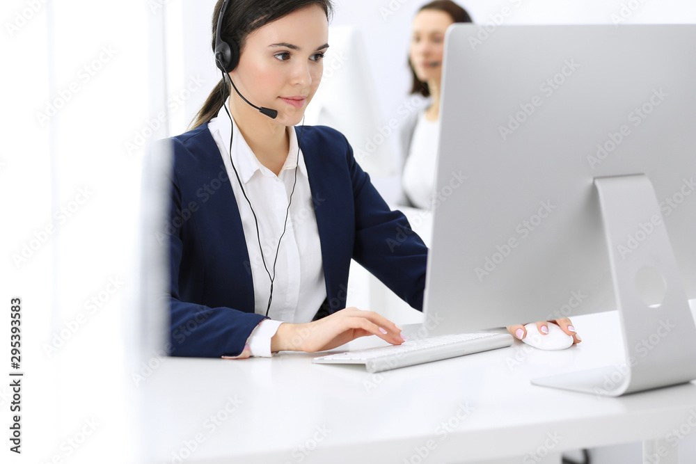 Call center. Beautiful woman receptionist sitting in headset at customer service office. Group of operators at work. Business concept