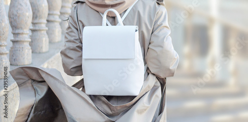 Fashionable bag close-up in female hands.Girl walks in the city outdoors. Stylish modern and feminine image, style. Woman in a raincoat, coat and with a white backpack on his shoulder. girl backs.