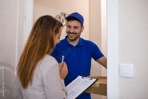 Receiving parcel - delivery man gives package to young woman. View of a Delivery man handing over a parcel to customer. Signing to get her package. Delivery man handing box to woman