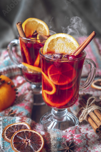 Hot mulled wine in two glasses, a winter scarf with a pattern, an orange on a gray background.