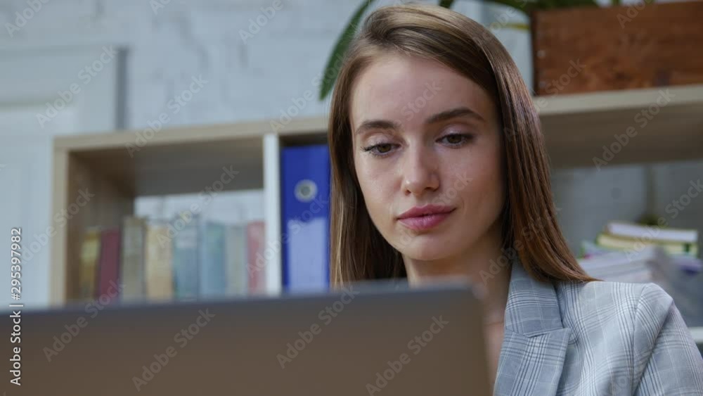 Portrait of beautiful smart young woman working by notebook in cozy office interior. Close-up pretty business girl behind laptop monitor.