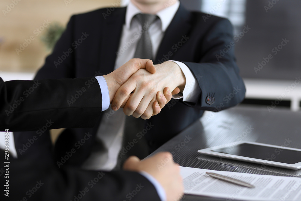 Businessman shaking hands with his colleague or partner above the glass desk in modern office, close-up. Unknown business people at meeting. Teamwork, partnership and handshake concept