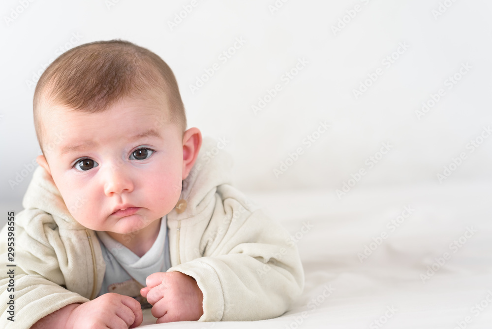 Beautiful and sweet newborn baby lying face down on the bed raising his head to look at the camera curiously.