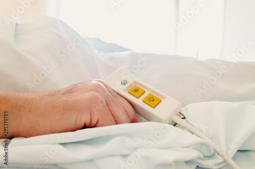 Older woman lying in hospital bed using the assistance command for help.