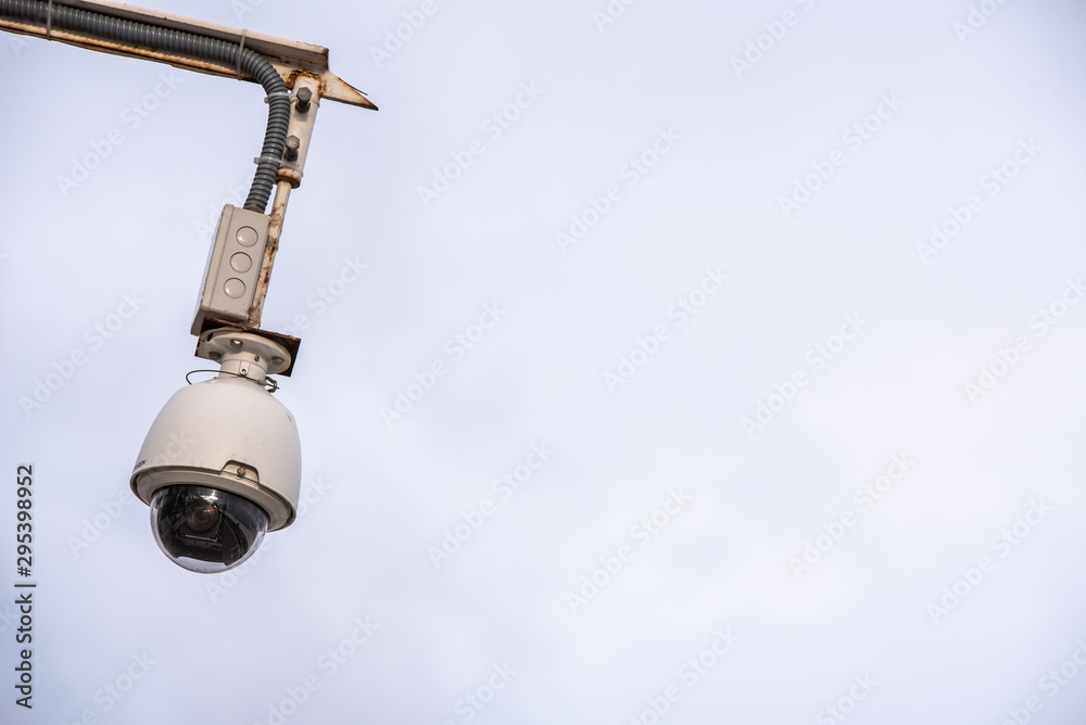 Security camera hung to monitor people in a city, isolated over blue sky and clear background with a lot of free copy space. Security camera hung to monitor people in a city, isolated over blue sky and clear background with a lot of free copy space.