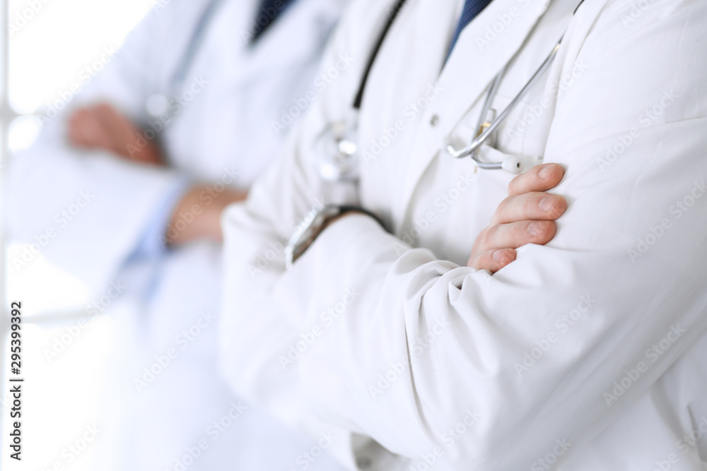 Group of modern doctors standing as a team with arms crossed in hospital office, close-up. Physicians ready to examine and help patients. Medical help, insurance in health care, best treatment and Group of modern doctors standing as a team with arms crossed in hospital office, close-up. Physicians ready to examine and help patients. Medical help, insurance in health care, best treatment and