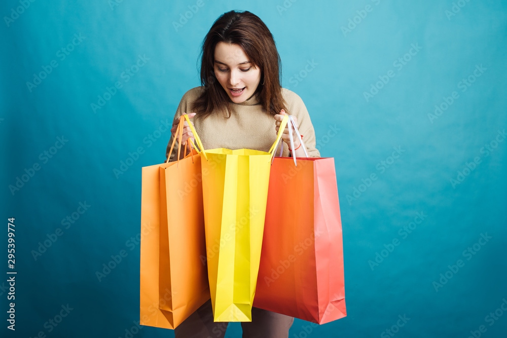Image of happy young girl standing on blue background with shopping bags Image of happy young girl standing on blue background with shopping bags