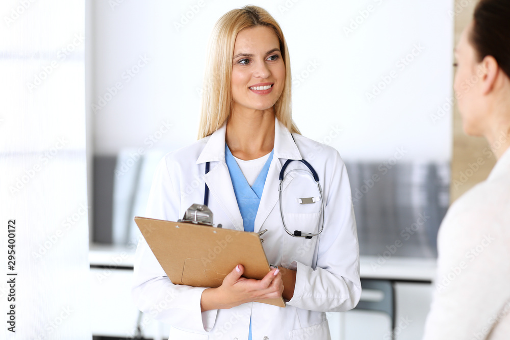 Doctor woman at work in hospital excited and happy of consulting female patient. Blonde physician controls medication history records and exam results while using clipboard. Medicine and healthcare Doctor woman at work in hospital excited and happy of consulting female patient. Blonde physician controls medication history records and exam results while using clipboard. Medicine and healthcare