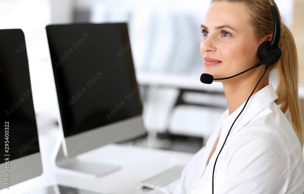 Call center. Happy and excited business woman using headset while consulting clients online. Customer service office or telemarketing department. Smiling blonde female operator at work Call center. Happy and excited business woman using headset while consulting clients online. Customer service office or telemarketing department. Smiling blonde female operator at work