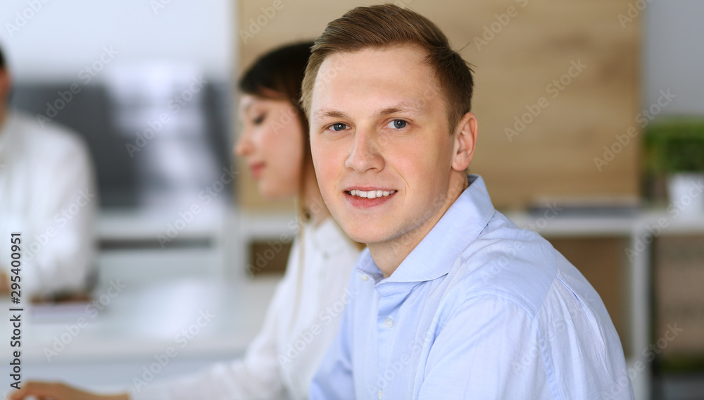 Cheerful smiling businessman headshot at work in modern office. Unknown casual dressed entrepreneur using pc computer while sitting with diverse colleagues at the background. Multi ethnic working Cheerful smiling businessman headshot at work in modern office. Unknown casual dressed entrepreneur using pc computer while sitting with diverse colleagues at the background. Multi ethnic working