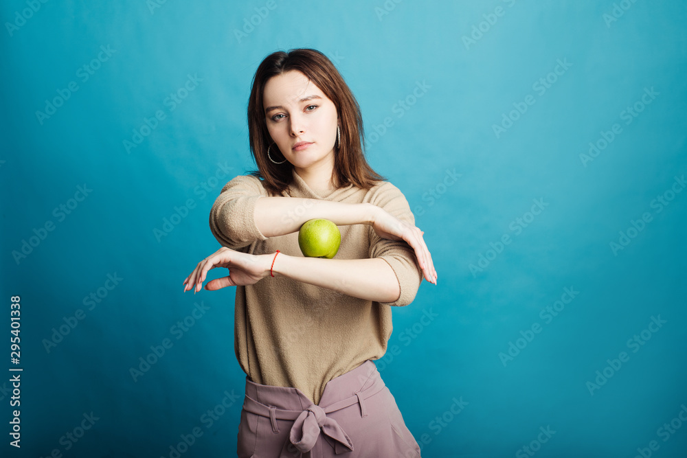 Image of a happy young girl standing on a blue background holding a green apple