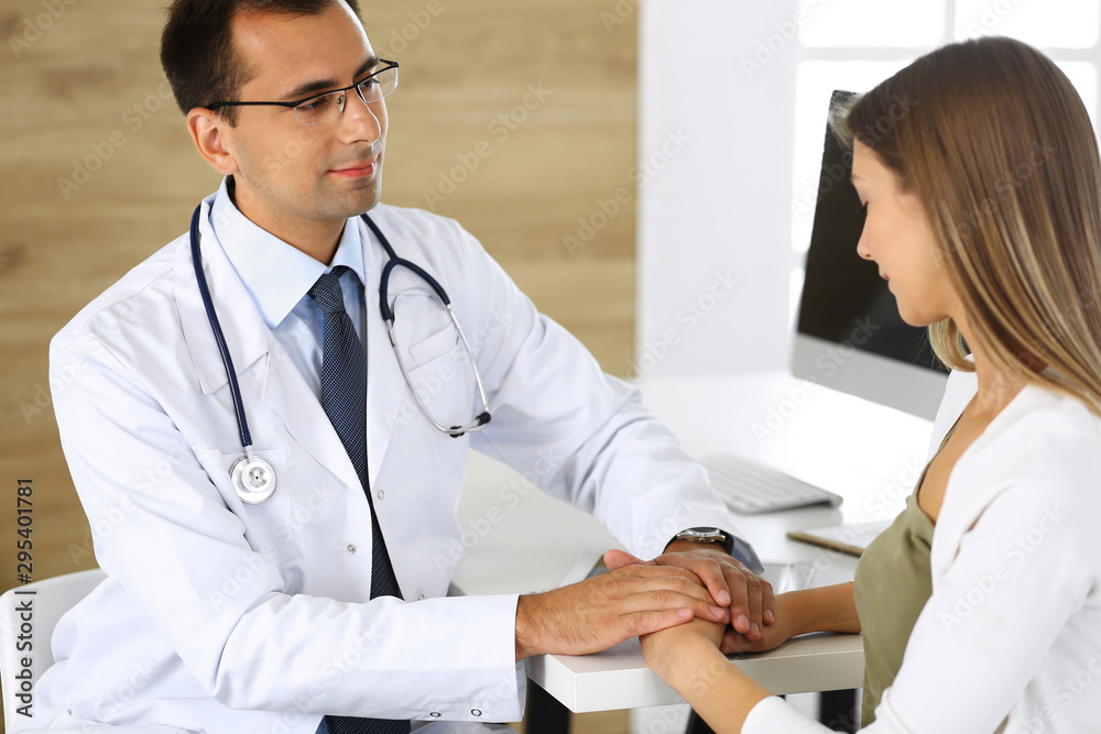 Doctor reassuring her female patient because of her first pregnancy fear while sitting at a desk in a clinic. Concept of comforting, empathy and best medical service Doctor reassuring her female patient because of her first pregnancy fear while sitting at a desk in a clinic. Concept of comforting, empathy and best medical service