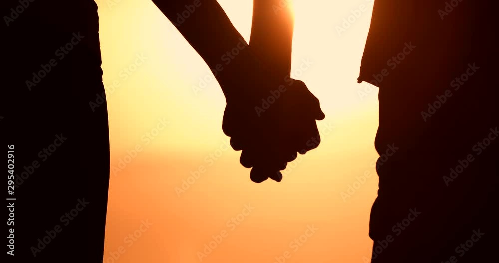 Silhouette of couple holding hands at sunset. Man and woman's hands slowly coming together. People love and relationships. 