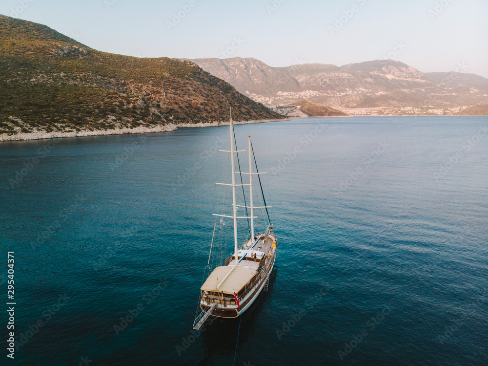 Traditional Turkish Gulets along the mountainous mediterranean coastline at sunset. The luxury boats dock against the cliffs for the night for shelter from the winds. Aerial drone shot from above. 