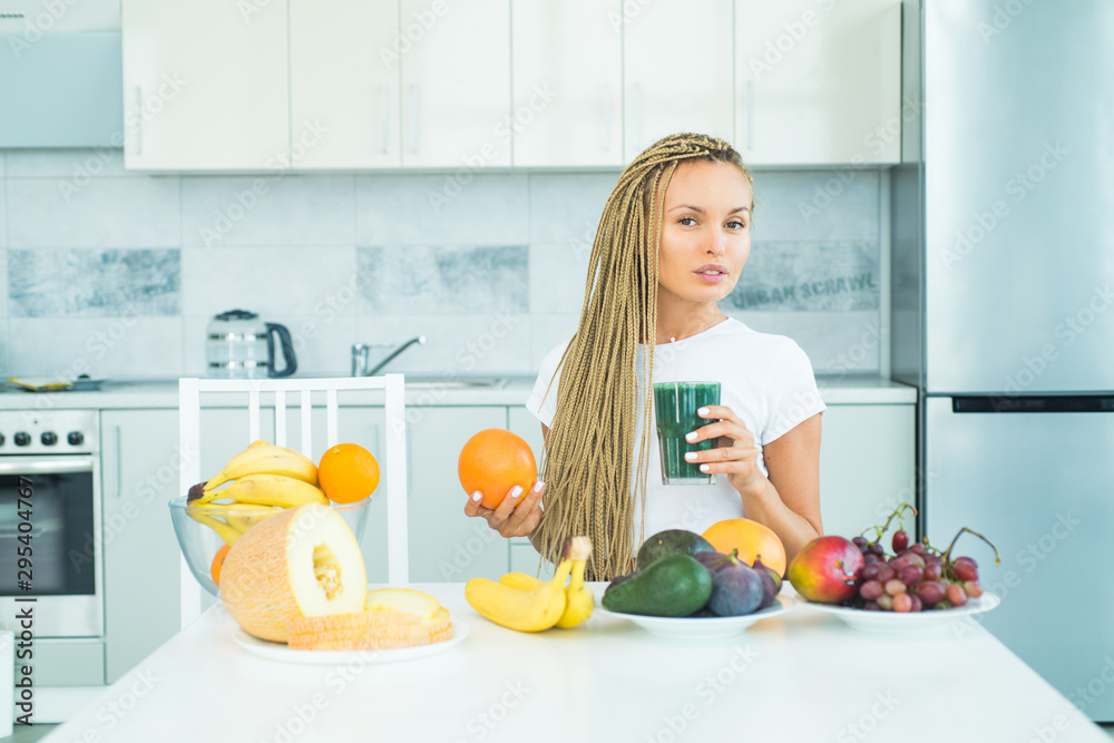 Smiling healthy woman drinks green smoothie in kitchen. Making smoothie menu. Fresh spirulina. Food supplements. Vegan concept. Well being and weight loss concept. Superfood.