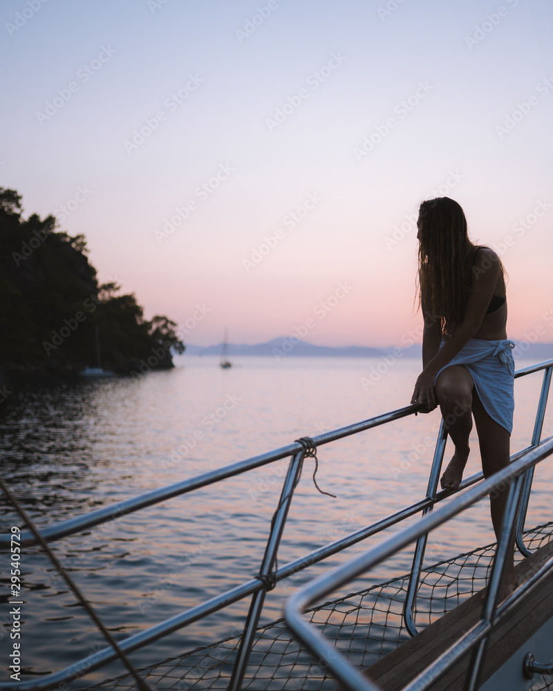 Naklejka premium Girl relaxing on the side of a yacht watching the sunset in the distance, thinking about life. Shot in antalya coastline, Turkey.