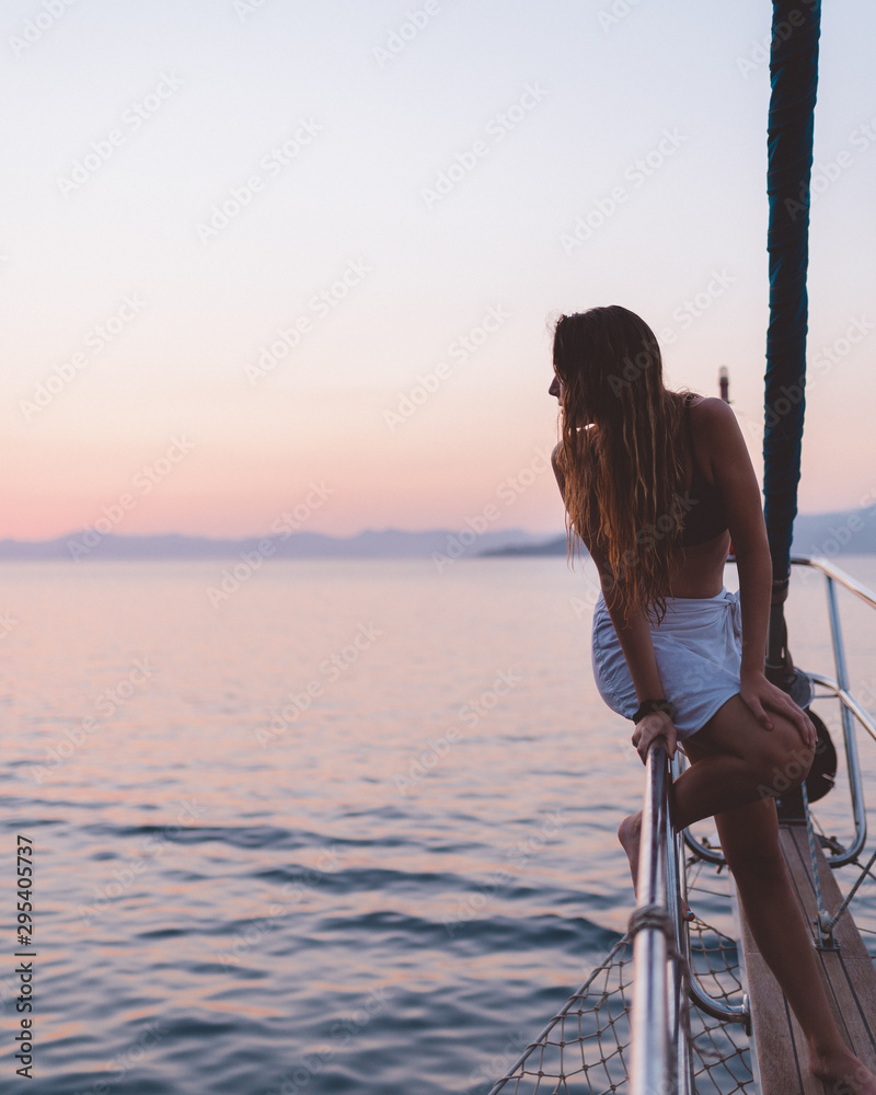 Obraz premium Girl relaxing on the side of a yacht watching the sunset in the distance, thinking about life. Shot in antalya coastline, Turkey. 