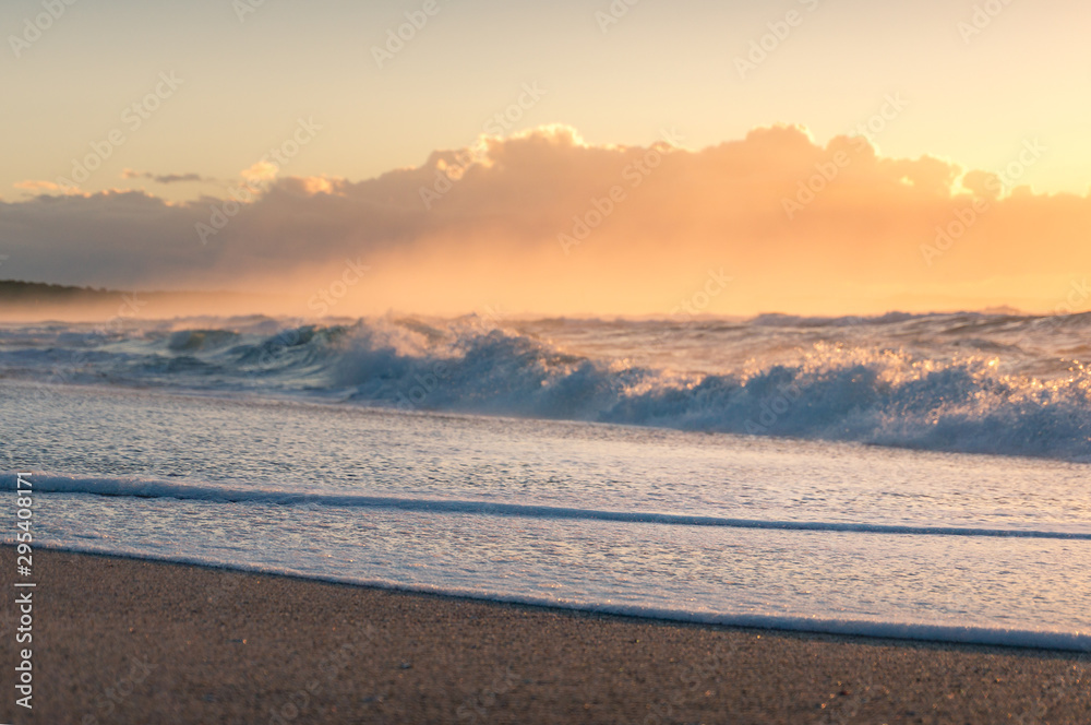 Close up of sandy shore with white foam of soft wave at sunrise