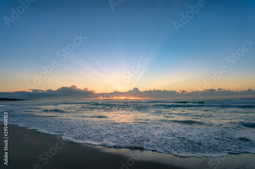 Beach landscape with soft waves on the shore and sun at sunrise