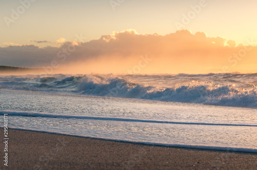 Close up of sandy shore with white foam of soft wave at sunrise