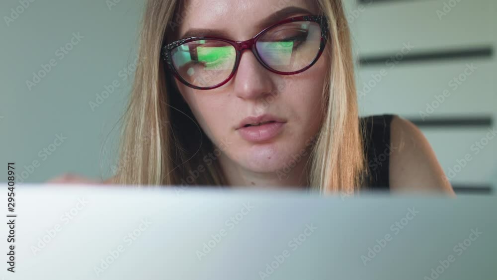 Busy girl in glasses working with laptop and smiling in office Busy girl in glasses working with laptop and smiling in office