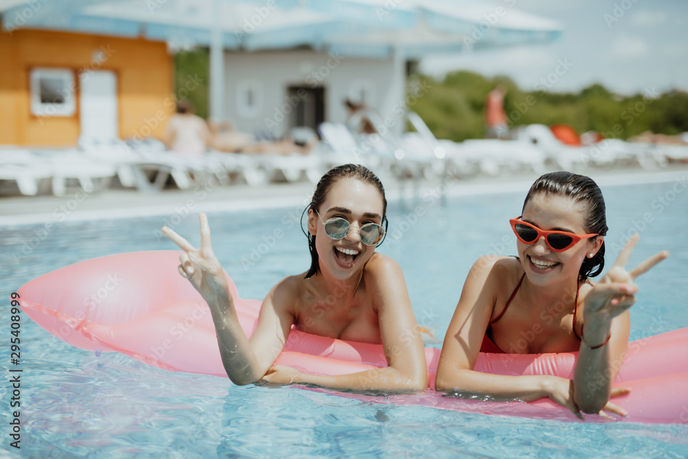 Two girls playing with water in the pool on inflatable pink mattresses
