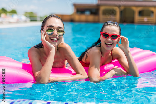 Two girls are swimming in a pool on inflatable pink mattresses © F8  \ Suport Ukraine